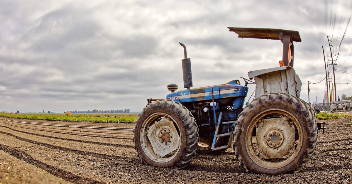 A small tractor parked on freshly worked farmland under a cloudy sky