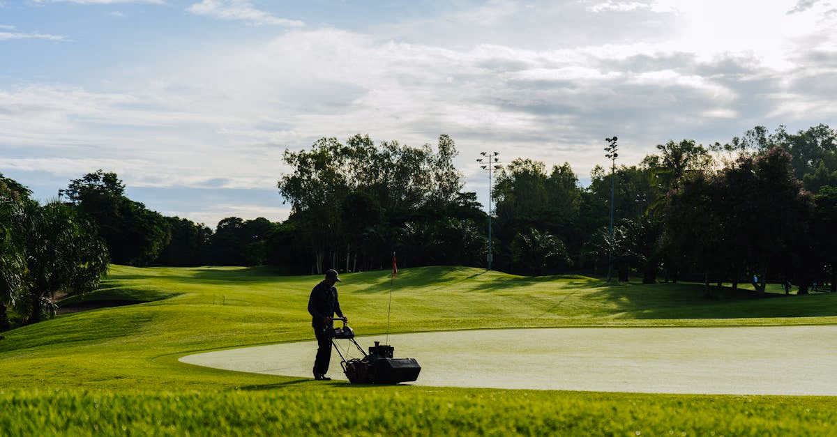 A groundskeeper mowing a golf course green with a ride-on cylinder mower