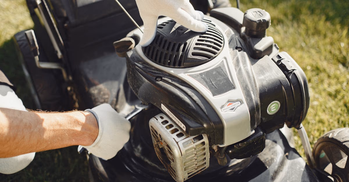 Gloved hands adjusting a petrol lawnmower outdoors